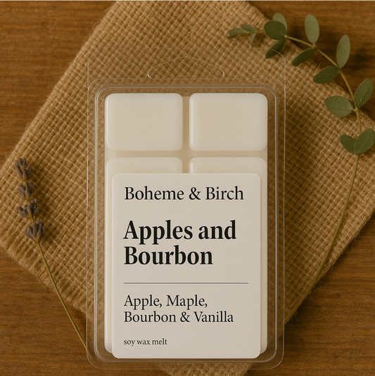 Boheme & Birch 'Apples and Bourbon' candle packaging on a wooden surface with a leafy branch.