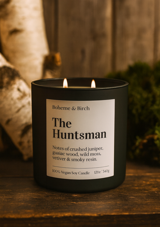 The Huntsman soy candle on a wooden table with birch trees and moss in the background